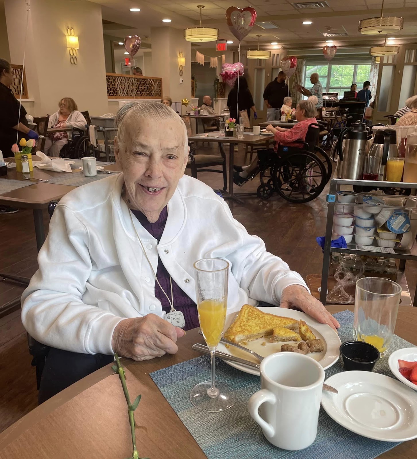 A woman smiling while eating French toast, sausage, and orange juice