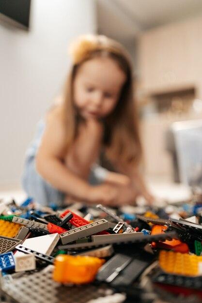 Funny, cute girl playing lego at home on the floor, focus on toys. First education role lifestyle