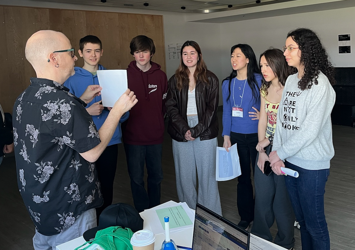 Les finalistes de la section française, Leïla Malo, Sara-Joelle Yao et Cynthia Li, visitent l'École secondaire publique de La Salle. Cynthia est photographiée en train de faire un exercice de poésie avec un enseignant et des élèves de La Salle. 