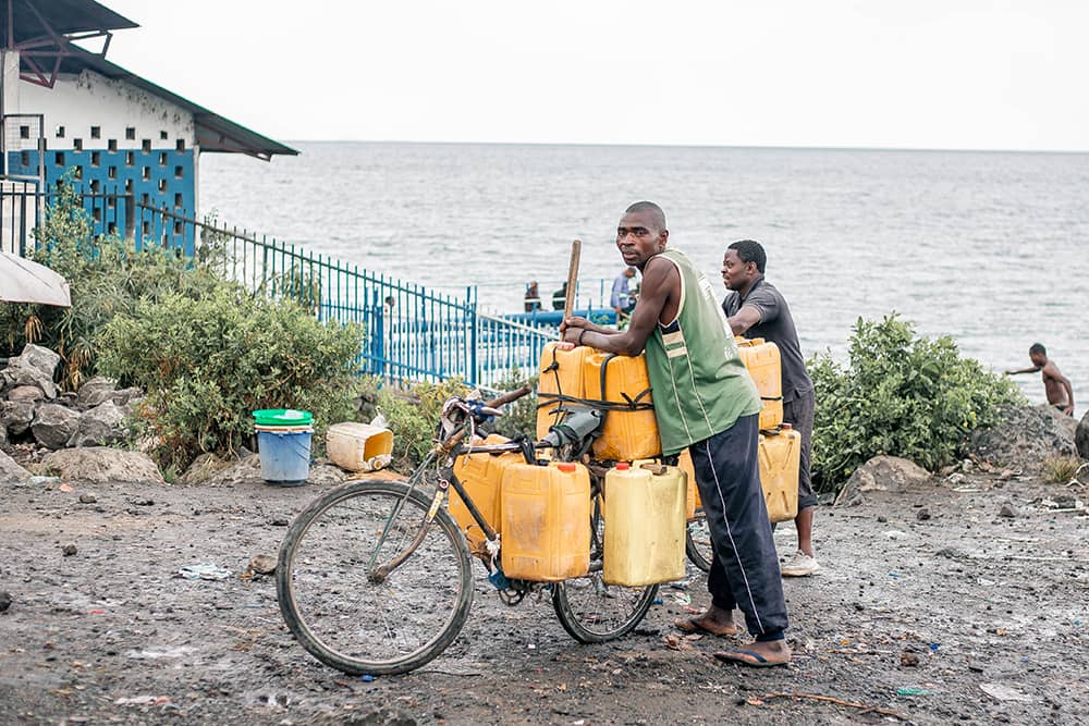 A man leans on a bike loaded with plastic containers filled with water from the vast lake in the horizon