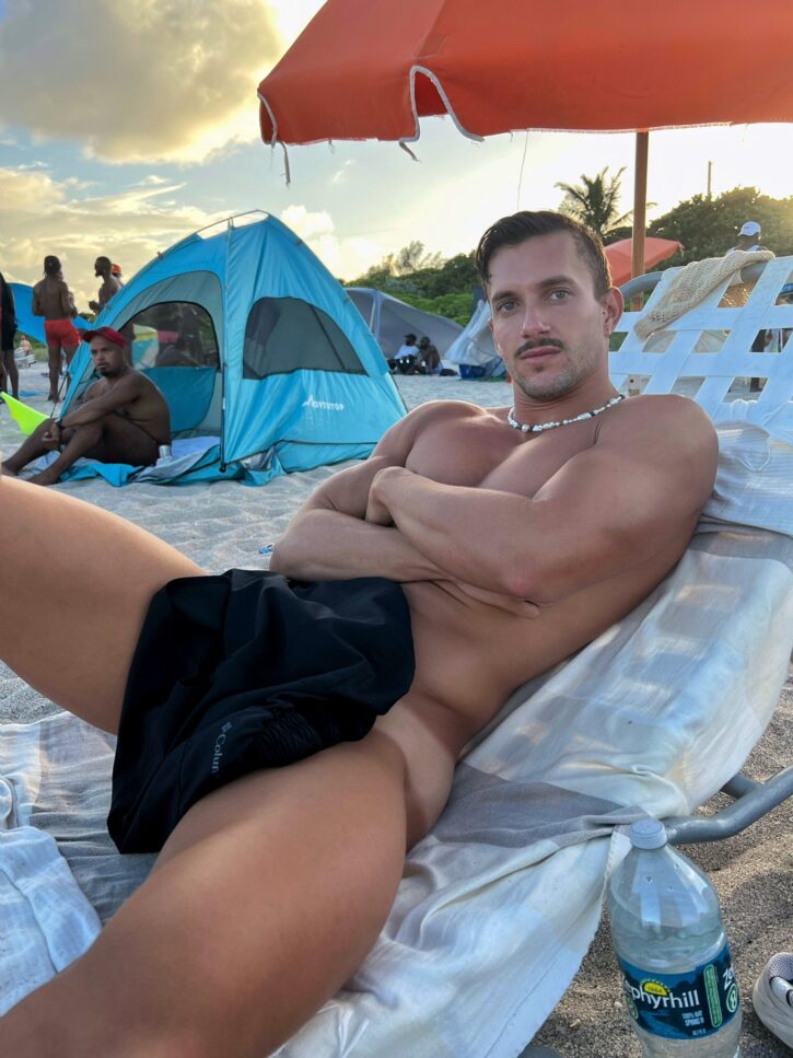 Eric Rmgr onlyfans creator naked at the beach covering his tanned bod with a black towel