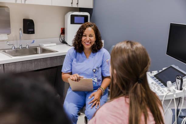 Female ultrasound tech smiles at unrecognizable couple Before performing the ultrasound, the mature adult female technician smiles at the unrecognizable couple. family nurse practitioner stock pictures, royalty-free photos & images