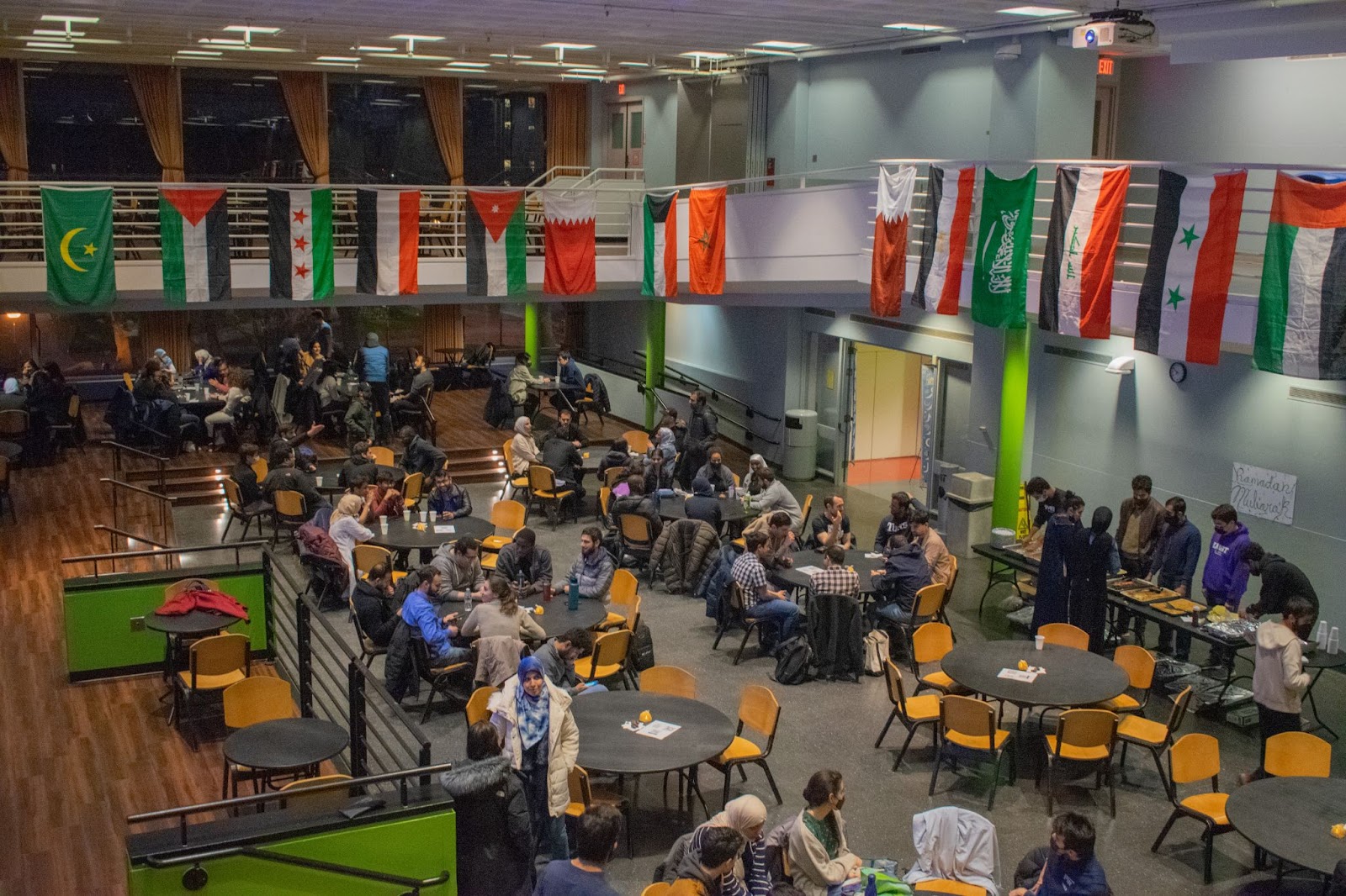 Students eat together in a large cafeteria decorated with flags.