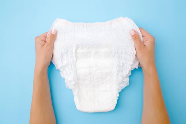 Woman hands holding white adult diaper on pastel blue background. Closeup. Point of view shot. Top view. Woman hands holding white adult diaper on pastel blue background. Closeup. Point of view shot. Top view. adult diaper stock pictures, royalty-free photos & images