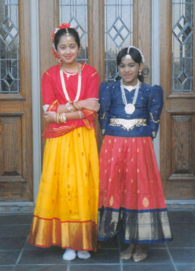 Two girls in traditional dresses standing in front of a door

Description automatically generated