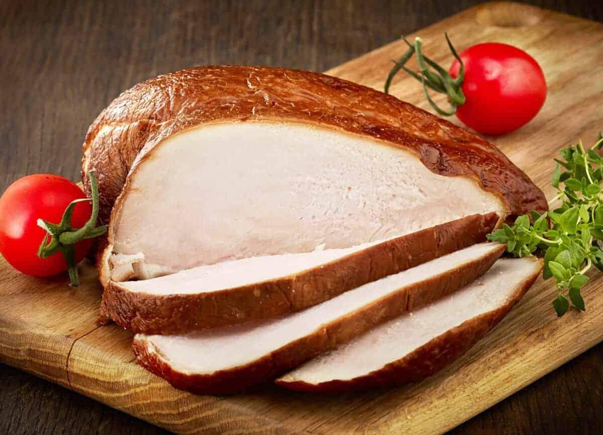 Piept de pui afumat și feliat pe o masă de tăiat cu roșii cherry