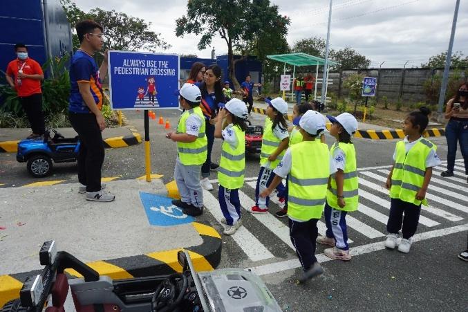 A group of children in safety vests standing in a crosswalk

Description automatically generated