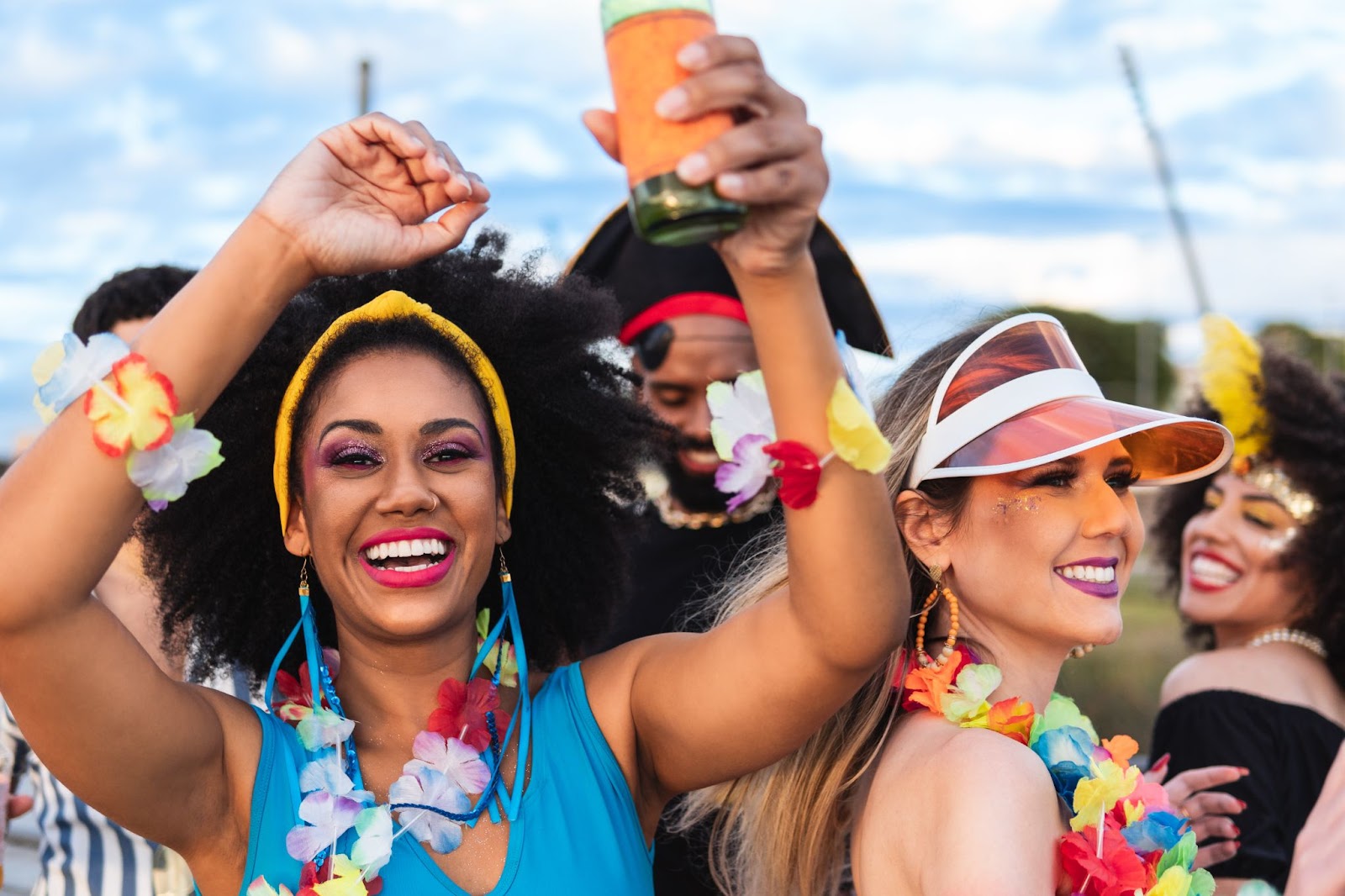 Jovens sorridentes reunidos em uma festa ao ar livre. Eles usam acessórios carnavalescos coloridos