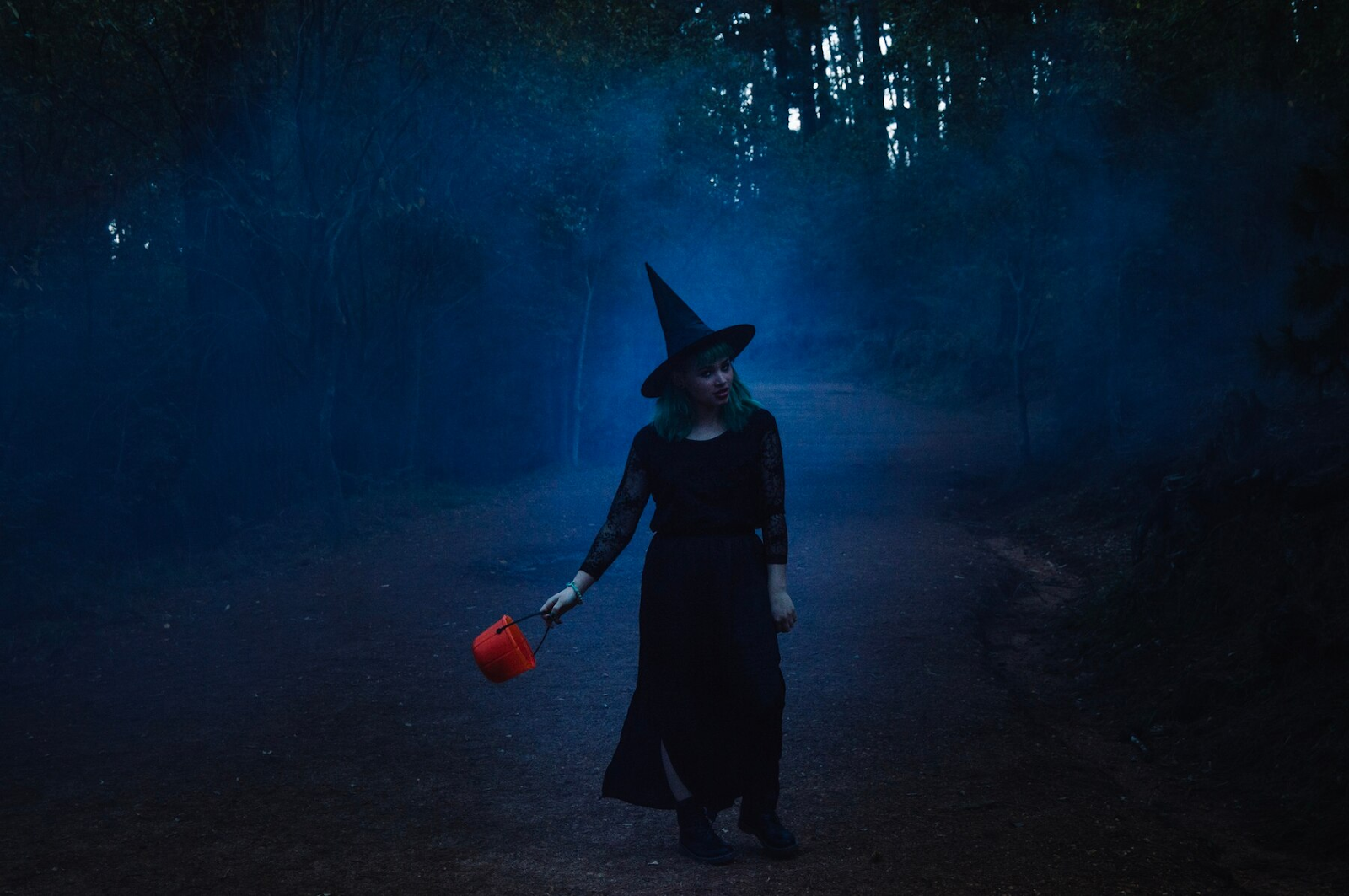 A witch holding an orange bucket on a misty path.