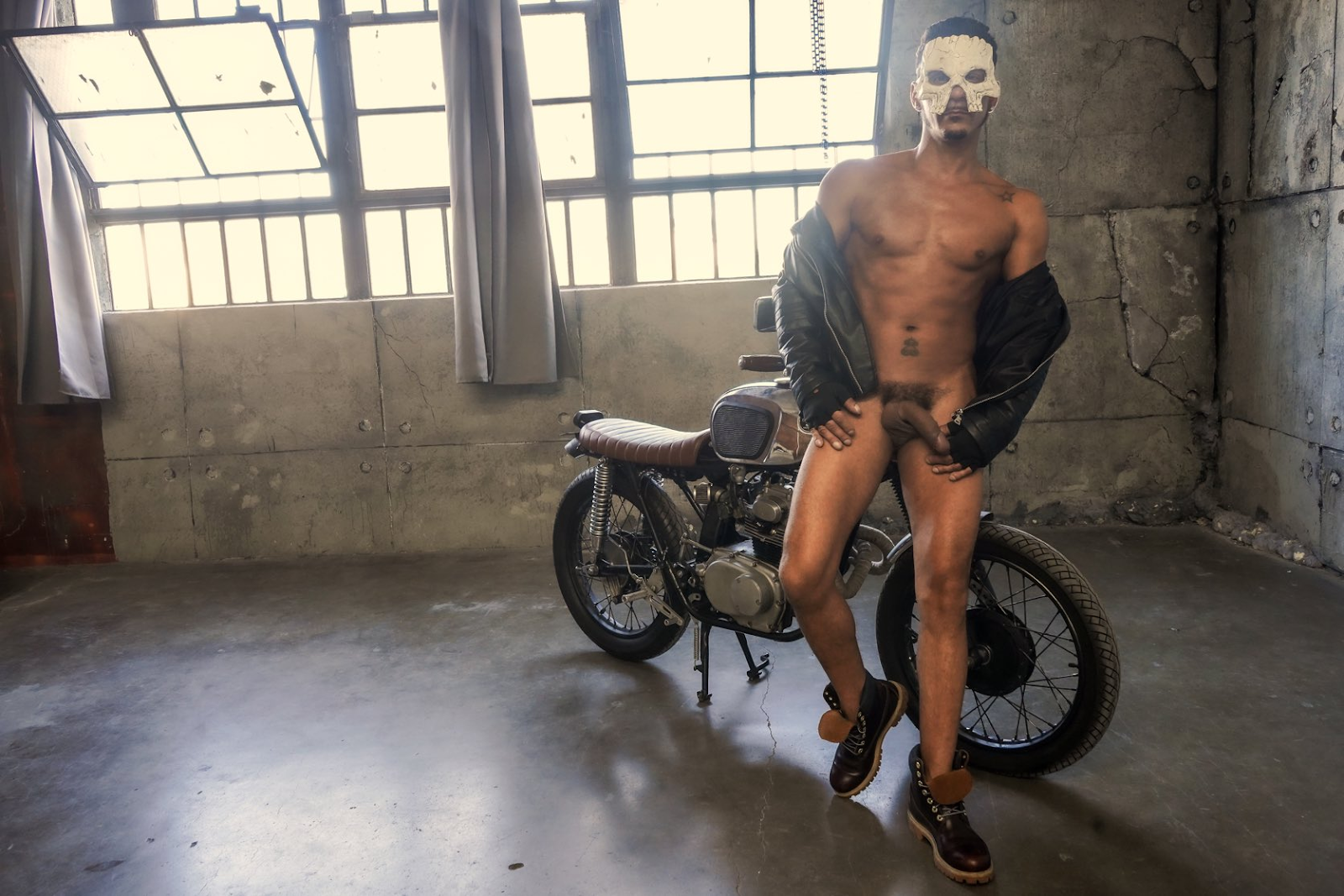 Cesar Xes wearing a leather jacket posing near a motorbike wearing no pants and touching his half erect dick
