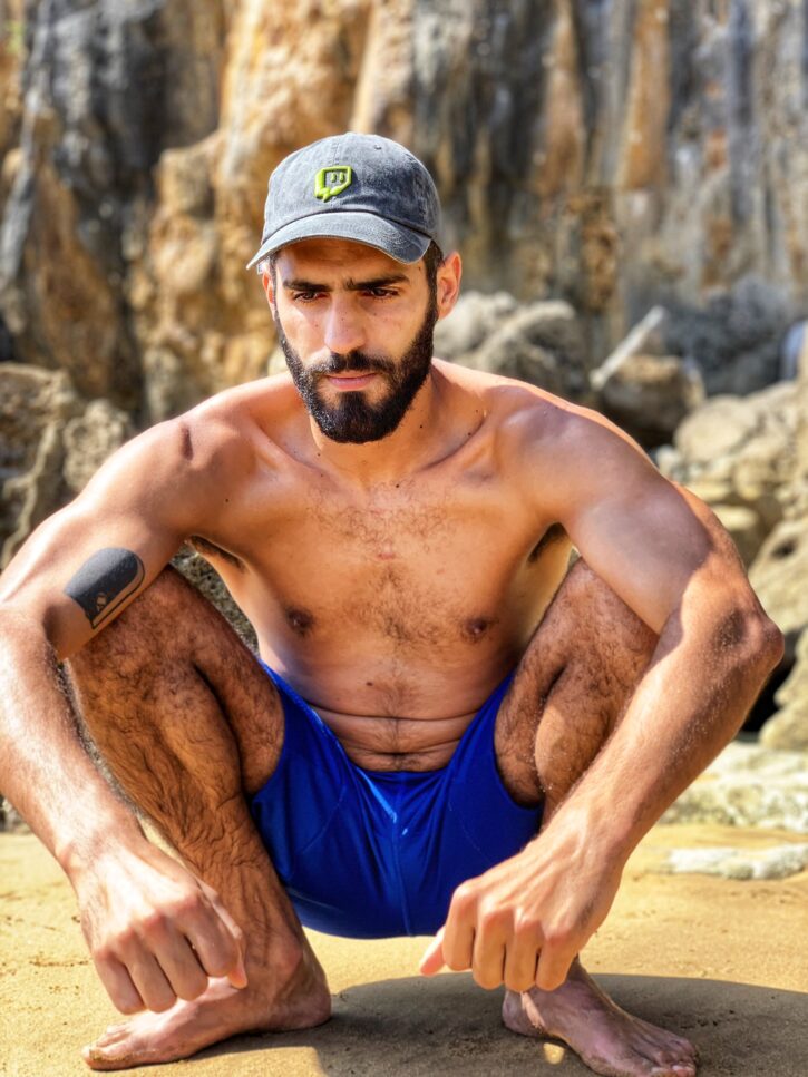 karim yoav kneeling shirtless outside in blue shorts in a crouch