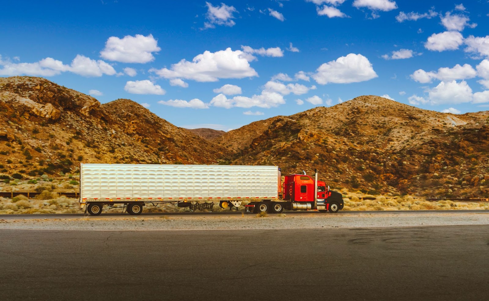 A semi truck with a trailer parked on the side of a road with mountains in the background