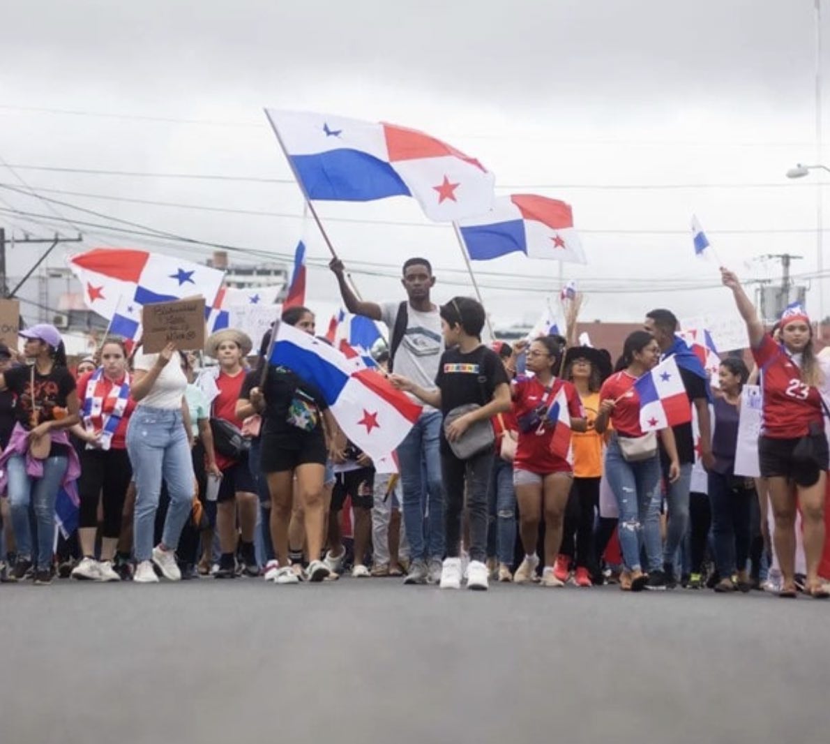 Protesters of all ages march towards the camera waving Panamanian flags
