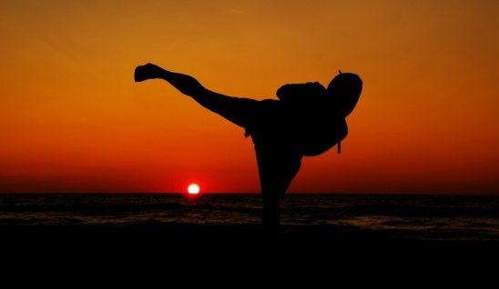 Person doing high kick against sunset on beach