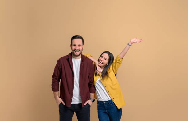 Cheerful young girlfriend with hand raised screaming and leaning on handsome boyfriend. Portrait of attractive couple dressed in shirts posing happily over beige background Cheerful young girlfriend with hand raised screaming and leaning on handsome boyfriend. Portrait of attractive couple dressed in shirts posing happily over beige background man happy stock pictures, royalty-free photos & images