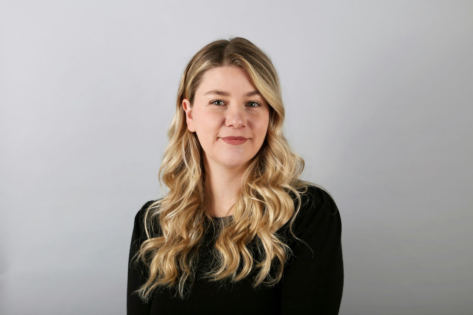 A woman in timeless black attire is posing in front of a white background to pose for her realtor headshots.