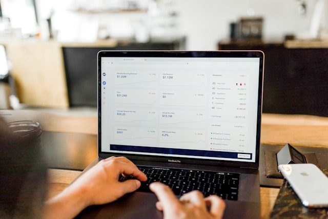 Person typing on a laptop with a financial analytics dashboard displayed on the screen.