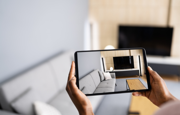 Hands holding a tablet displaying a virtual view of a living room, showcasing modern real estate market technology.