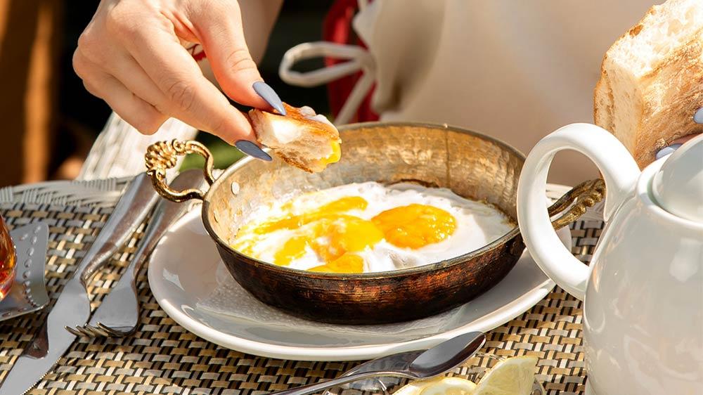 Strange French traditions: woman eating sunny side up eggs in a brass pan and dipping her baguette in the yolk