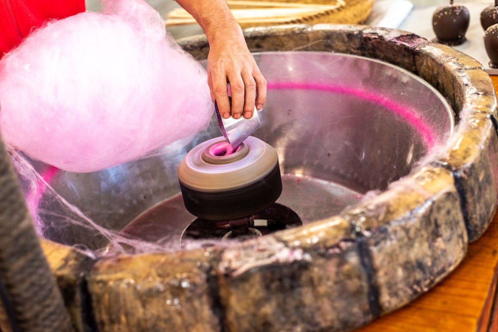 A vendor adds more sugar as he forms a pink cotton candy from the machine.