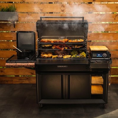 Traeger Timberline with food on all three grills and smoke surrounding.