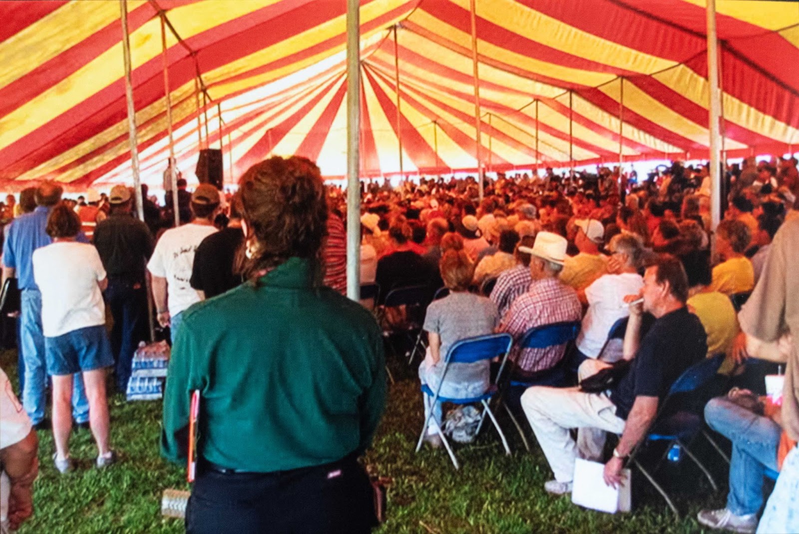 Photo of a crowd of people meeting under a white-and-red-striped tent 