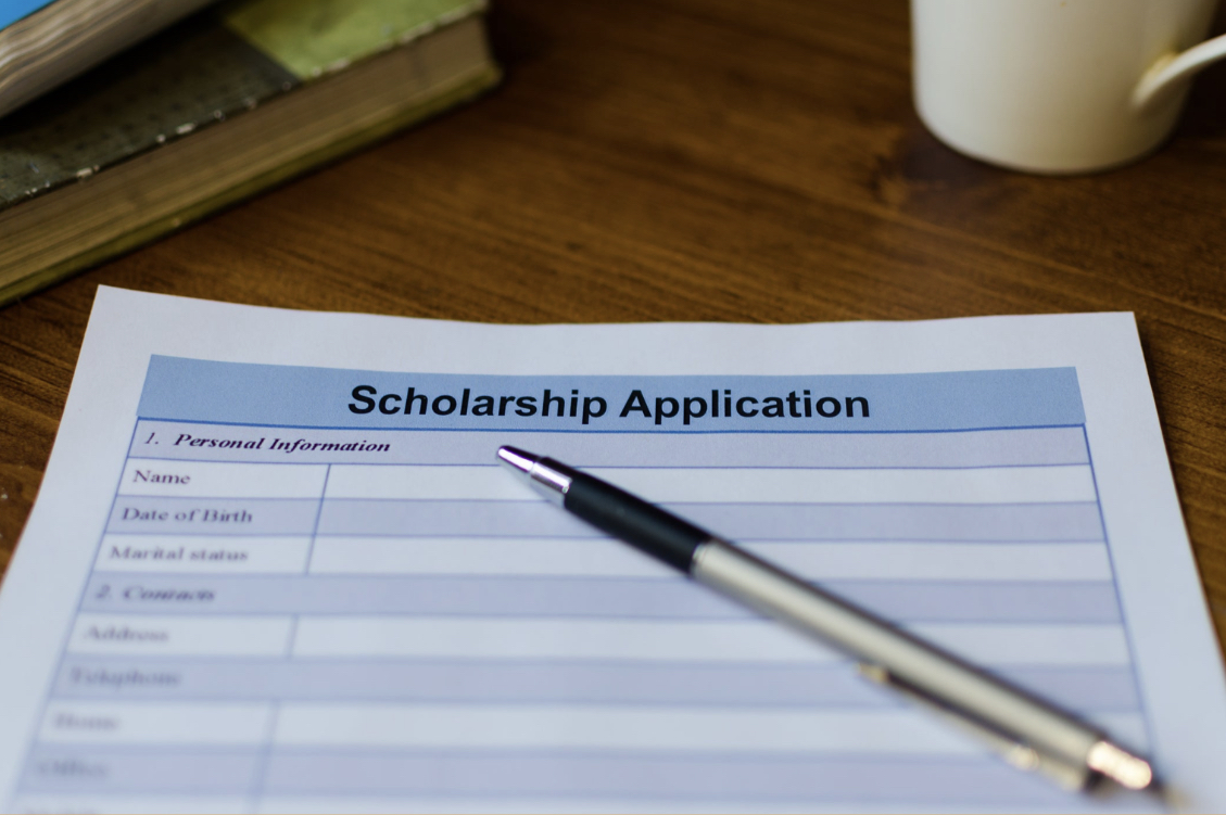 A pen sits on top of a blue scholarship application - The Best Scholarship Websites For Finding Money