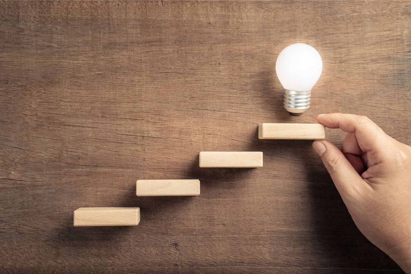 wooden blocks in brown background with lightbulb and hand