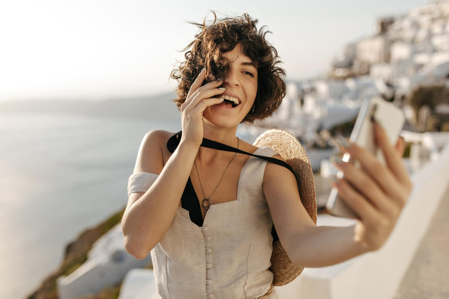 A lady in beige dress taking a selfie in a Greek city.