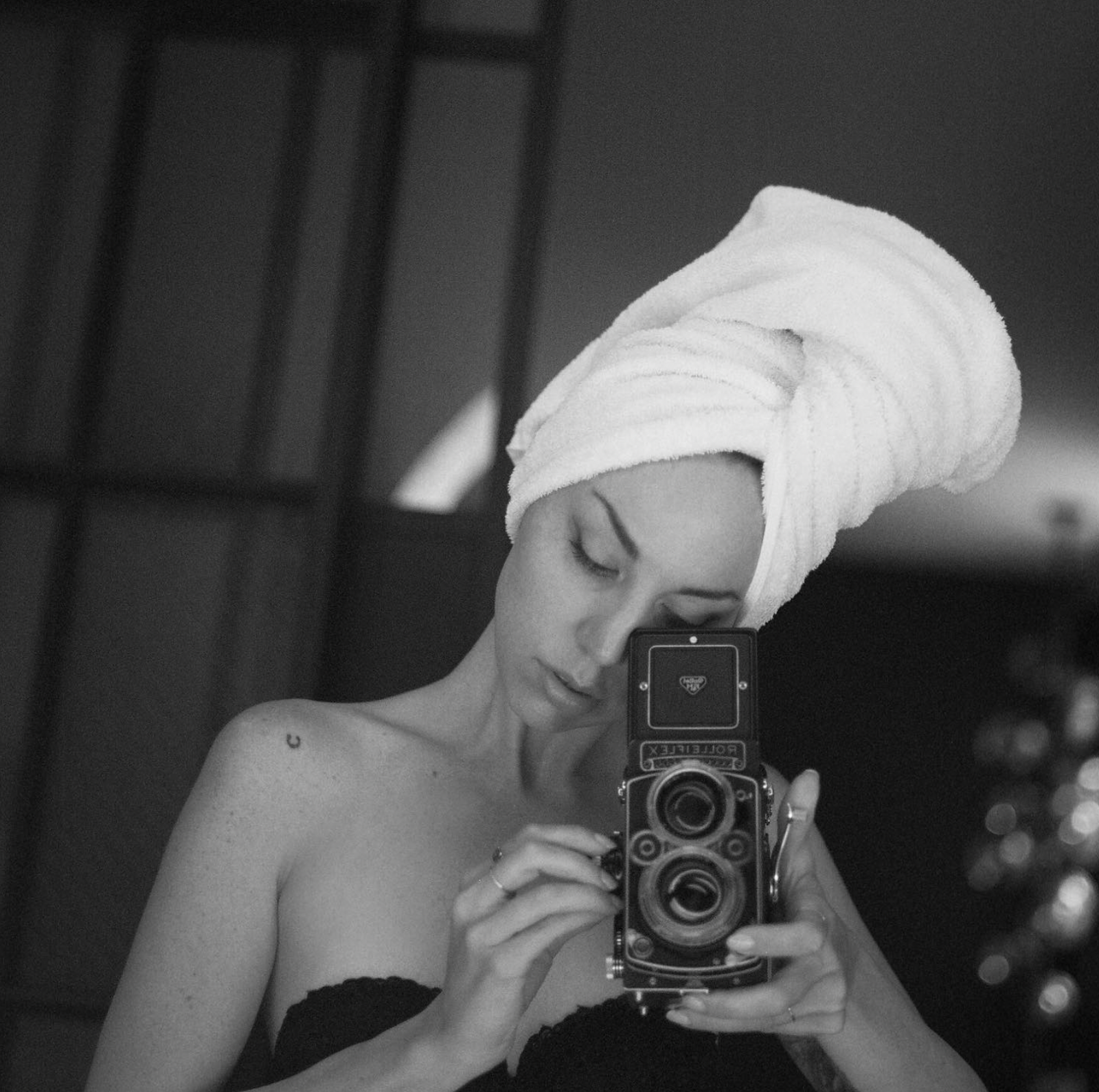 A black and white self portrait taken by photographer Allister Ann of her looking through a vintage camera with a white towel on her head.