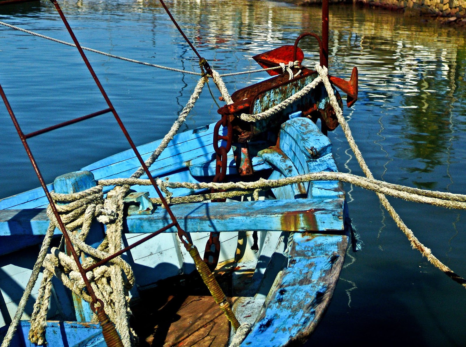Tradicional canoa caiçara, uma pequena embarcação feita de madeira e pintada em azul e branco. Ela está vazia e flutua em águas escuras.