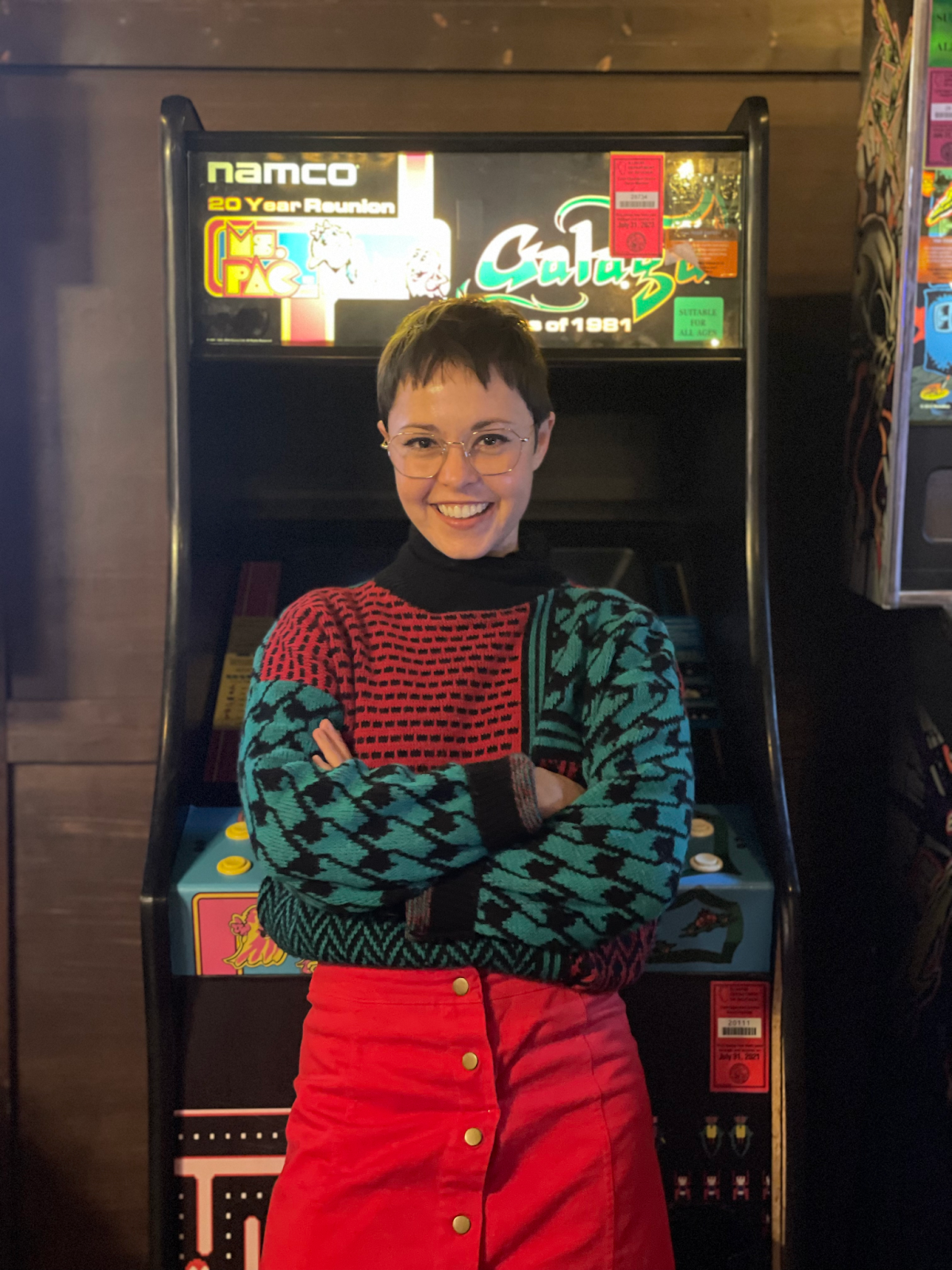 Oh hi, it's me Lauren standing in front of my favorite arcade game, Galaga, in a thrifted 90's patterned sweater and red button up skirt.