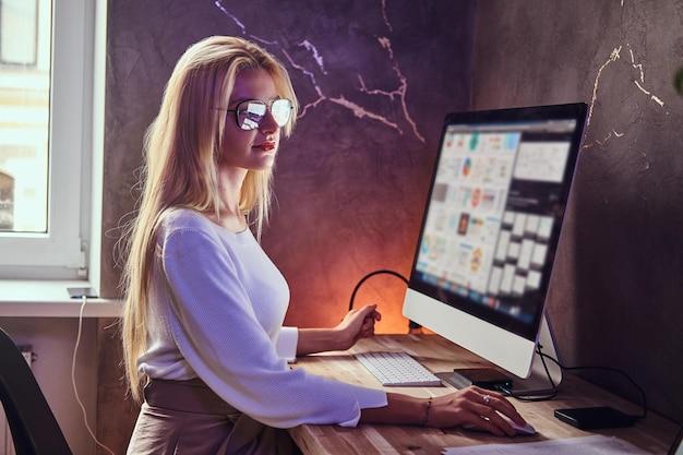 Attractive blond girl is studying at her modern room using computer.