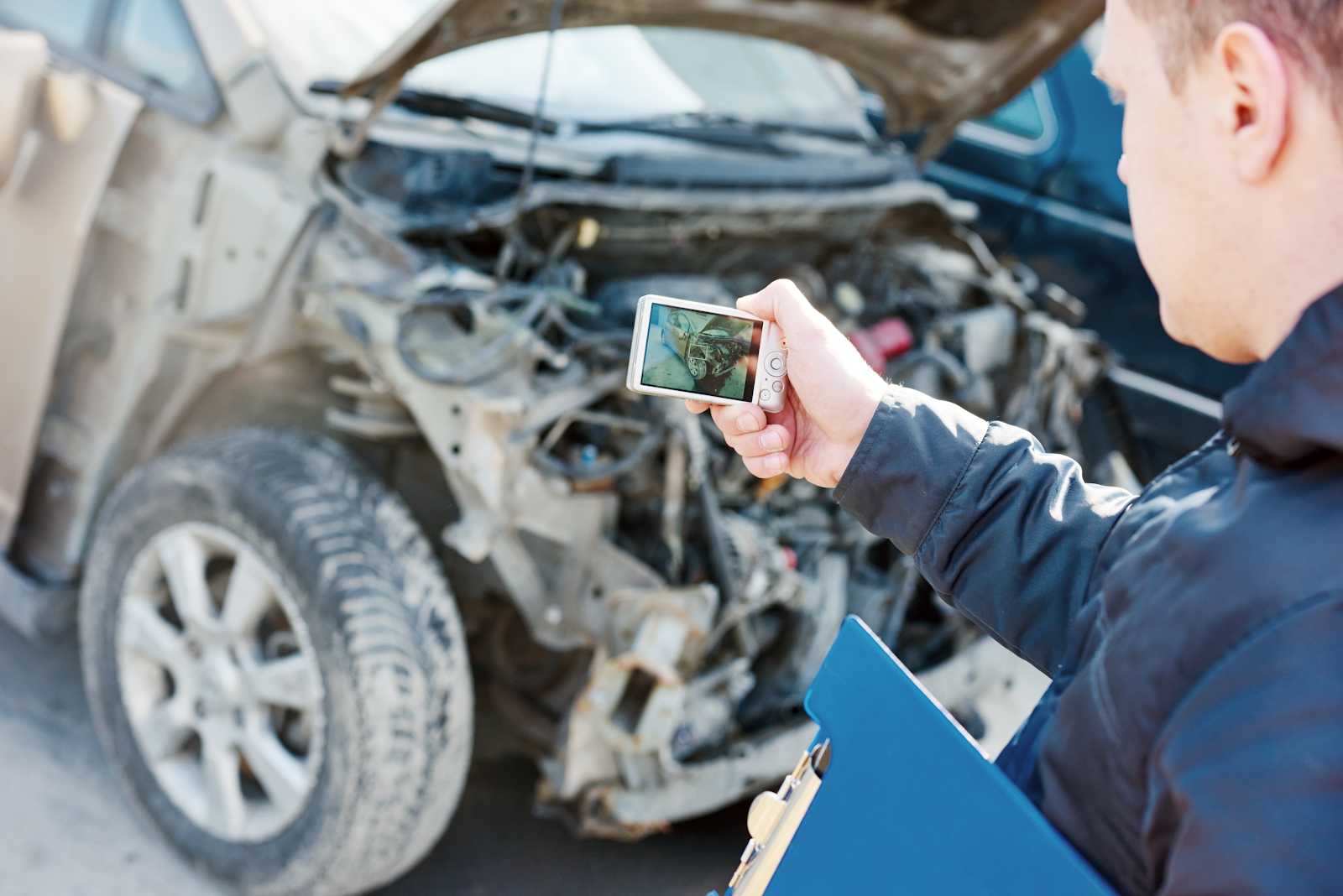 insurance company adjuster taking a picture of a damaged car after a car accident