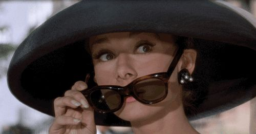 Imagem do filme "Bonequinha de Luxo": Holly Golightly abaixando os óculos escuros e arregalando os olhos para ver melhor.