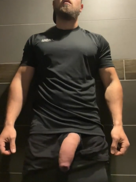 Max Small standing against a wall wearing athletic wear with his hard fat cock peeking out of his shorts