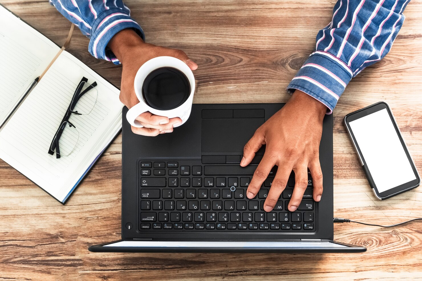 Overhead shot of a person drinking coffee and using his laptop.