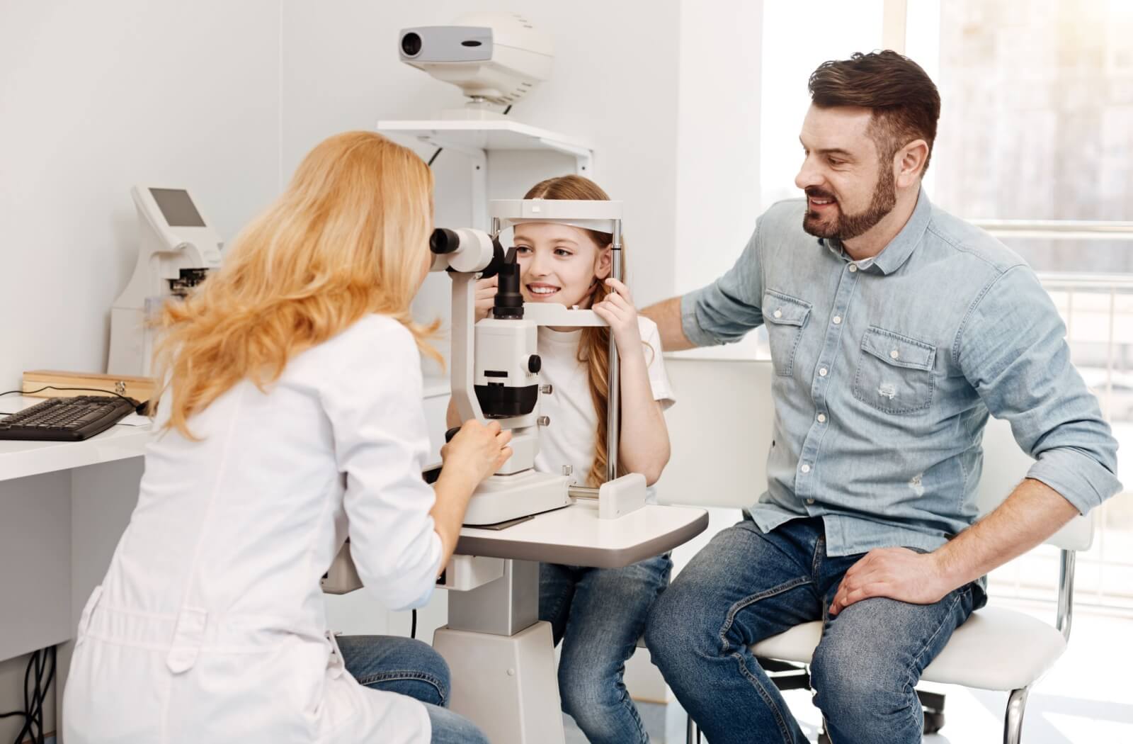 A child undergoing an eye exam. Her dad is beside her to emotionally support her.
