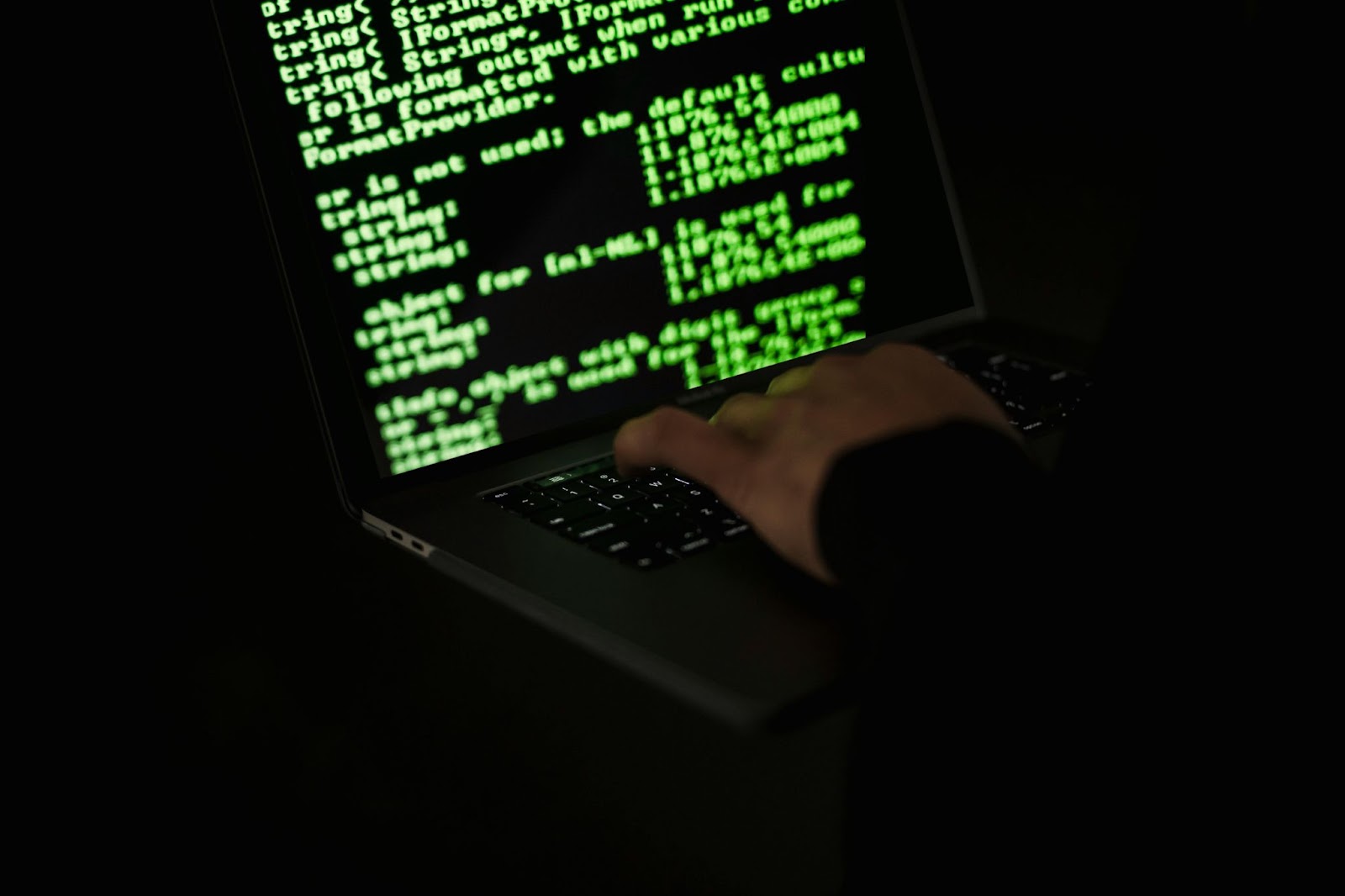 A person typing on a backlit keyboard in a dark room with a computer screen displaying the text