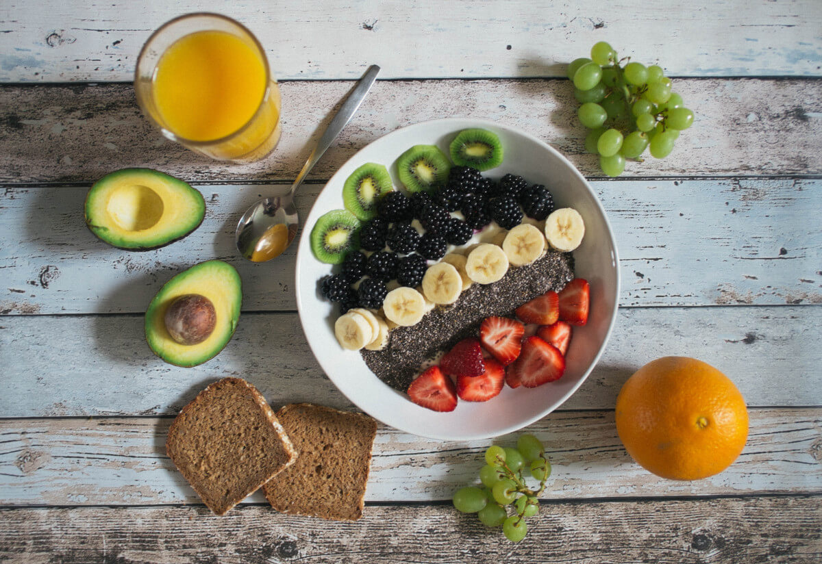 bowl of fruit on a rustic table with avocado and whole grain toast