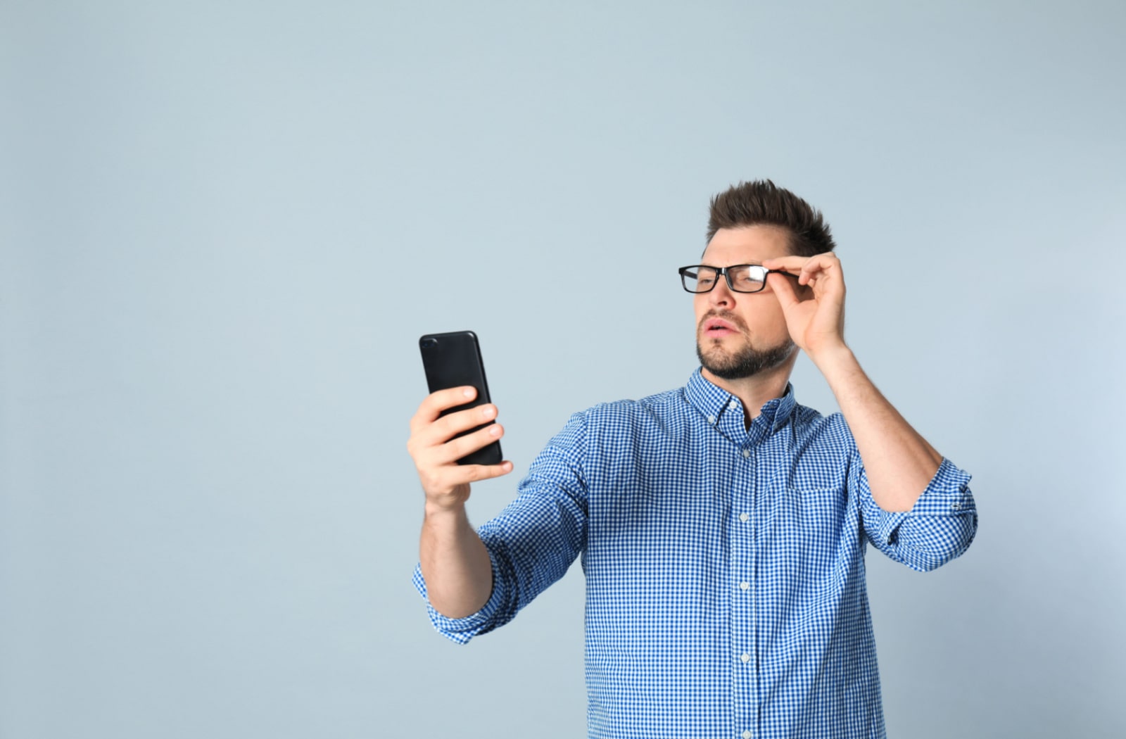 A man with hyperopia struggles to see his phone screen up close, so he is holding his smartphone farther away from his face