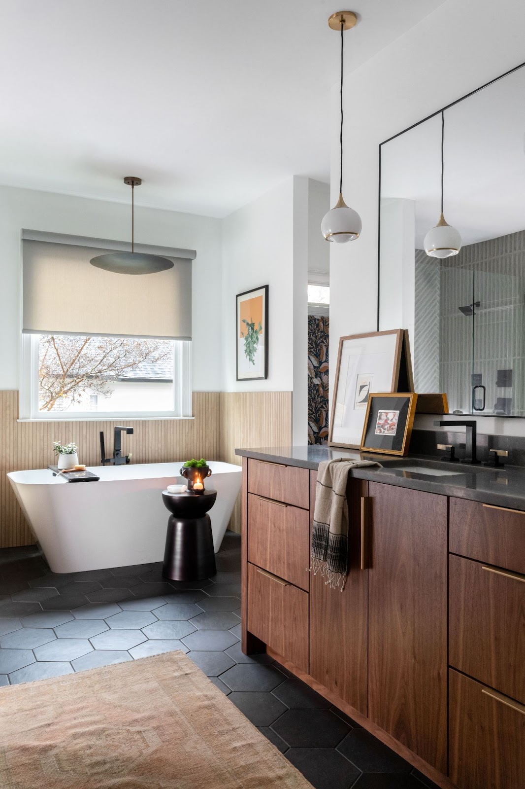 Cozy bathroom with wood cabinets, black tile flooring, white soaking tub, and artwork. 