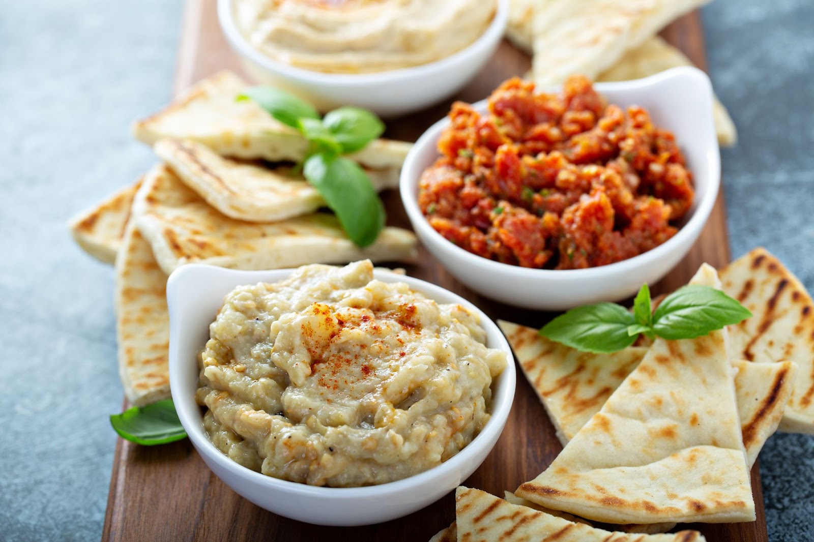 Close up of a Mediterranean Mezze Board featuring a wooden cutting board topped with a variety of dips and pita bread. This is one of many great appetizer themed board presentation ideas.
