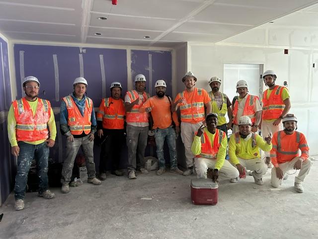 A group of men in safety vests and helmets posing for a photoDescription automatically generated