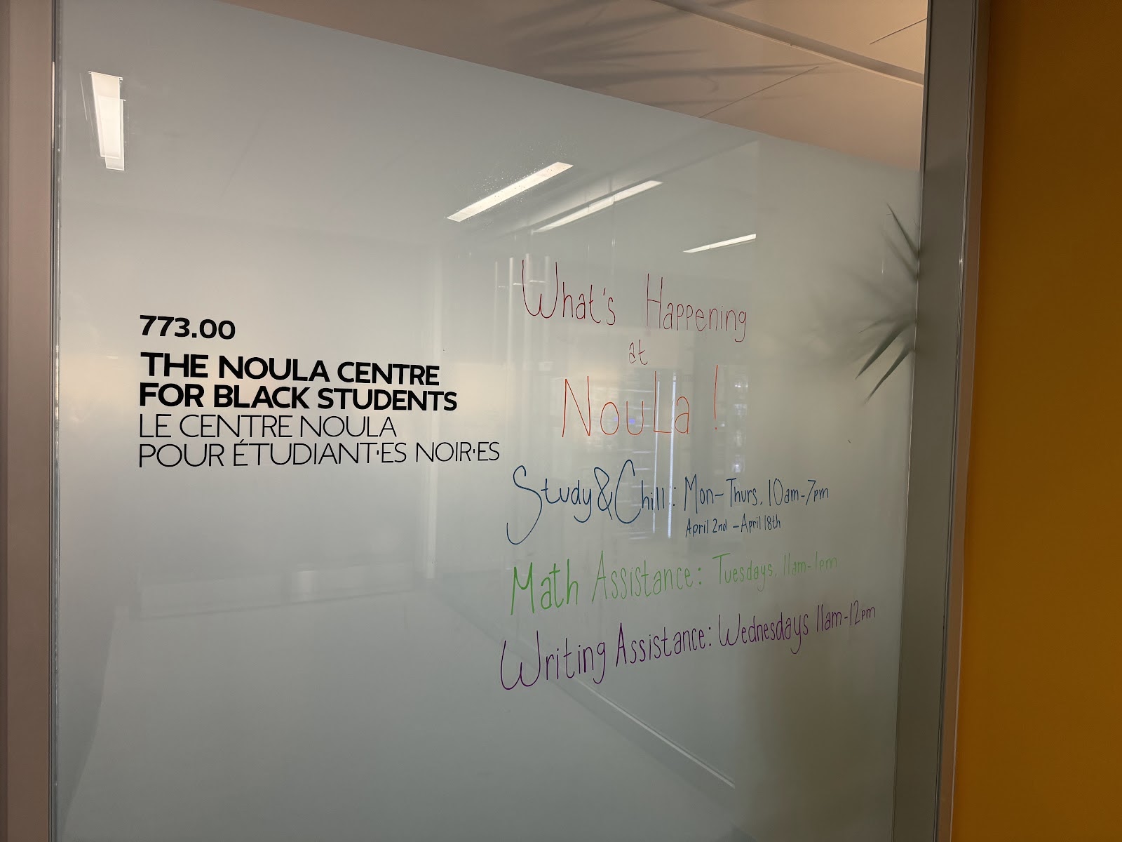 A frosted glass wall which says “773.00 THE NOULA CENTRE FOR BLACK STUDENTS”. There are also some events written in colourful markers.