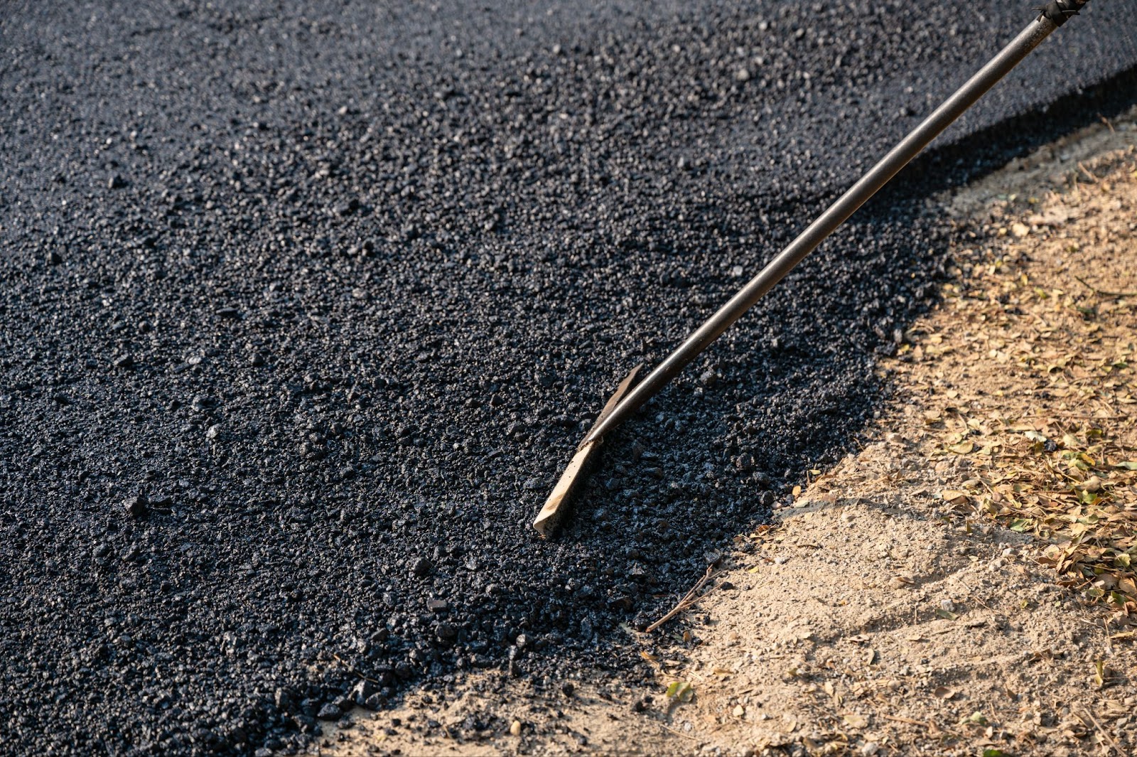 A close-up of a construction worker's tool evenly spreading hot-mix asphalt, accurately leveling the road surface.