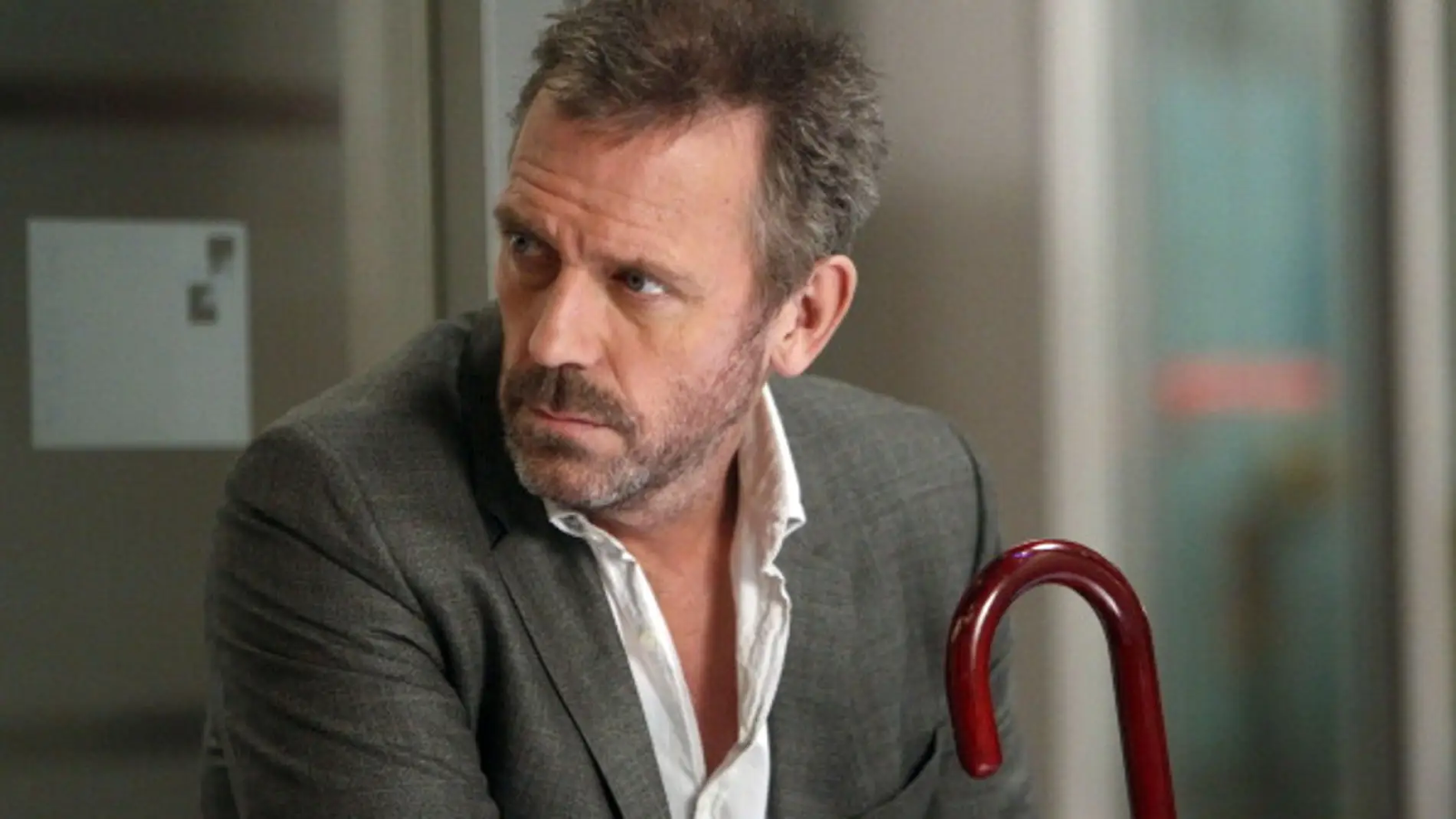 Dr. House (Hugh Laurie) observa hacia un lado con su bastón en mano.