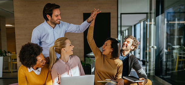 equipe de trabalho sorrindo, homem e mulher batendo as mãos em forma de comemoração enquanto trabalham