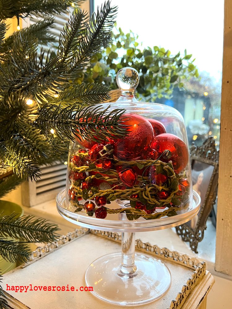 red baubles tucked in a glass cake stand with a christmas tree looking over a garden