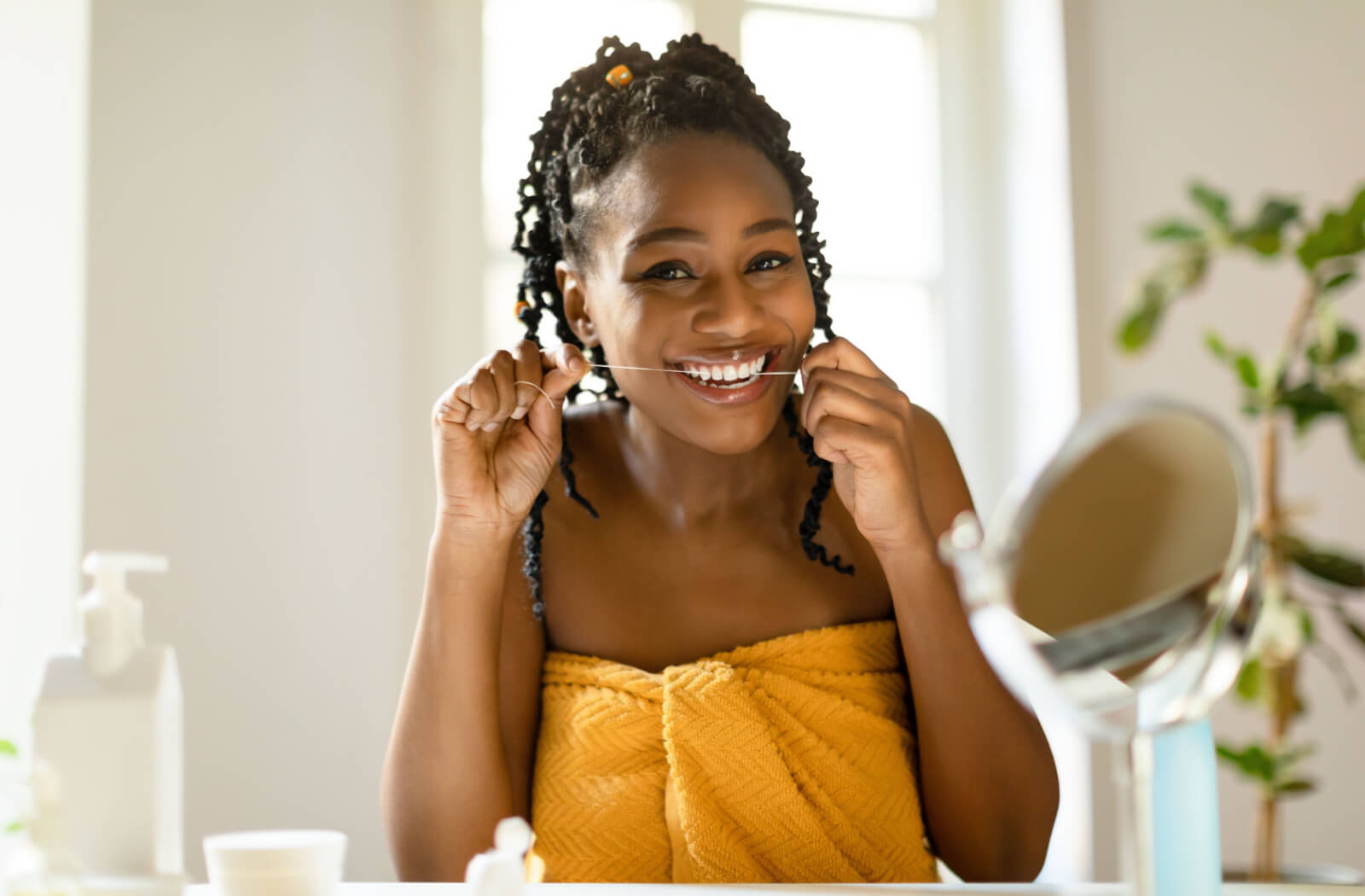 A woman flossing her teeth in front of a bathroom mirror.